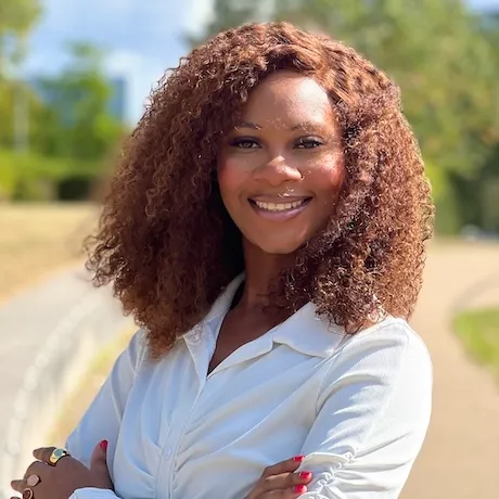 Ifeoma Nwosu smiling outdoors on a path, arms crossed, wearing a white button-front shirt.