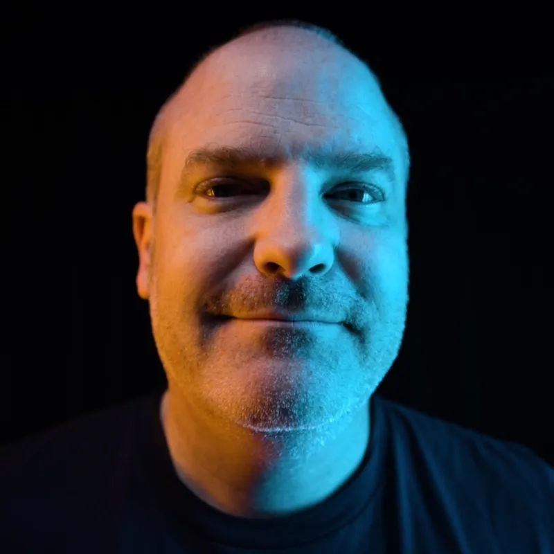 Jim Bennett in a close-up portrait lit in blue and orange against a dark background.