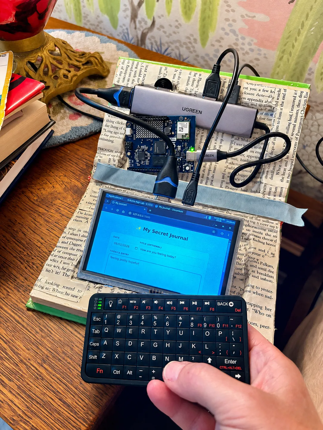 A hollowed-out hardcover book with a touchscreen embedded in the pages, showing a 'My Secret Journal' web app with a date, title, and a text entry. A small keyboard sits beside it.