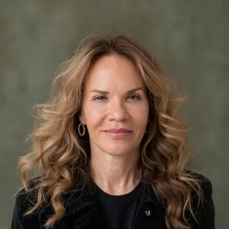 Laylah Bulman smiling in a studio portrait, wearing a black top against a muted green backdrop.